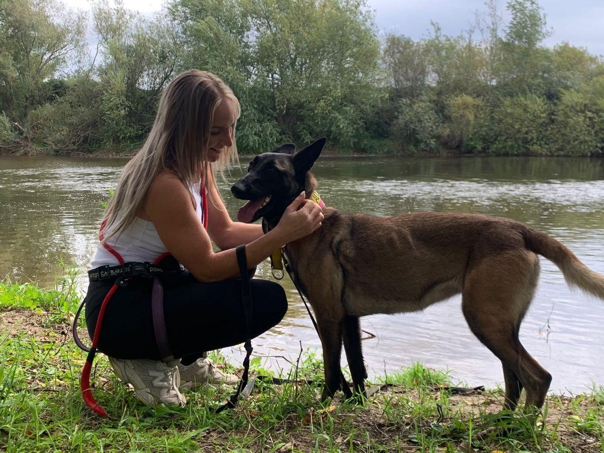 Cheryl crouched by the river giving a Malinois a fuss